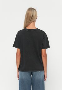 Black cotton t-shirt with a relaxed fit, short sleeves, and a round neckline. The back shows visible stitching and a textured finish.
