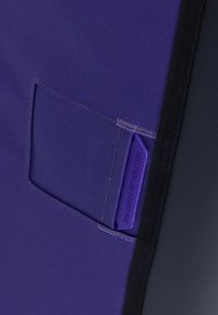 Borsa in tessuto viola con superficie testurizzata, dotata di una piccola tasca orizzontale e di un'etichetta con la scritta "INFORMAZIONI SUL PROPRIETARIO DELLA BORSA" in viola abbinato.