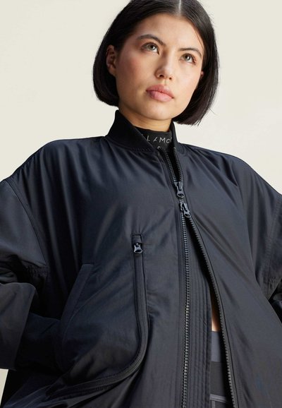 Černá bomber bunda s předním zipem, žebrovaným límcem a bočními kapsami. Hladká látka s matným povrchem; volný střih a oversized design.