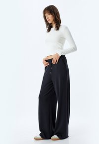 Zwarte wijde broek van zachte stof met een trekkoord in de taille en zijvakken, gecombineerd met een aansluitend wit longsleeve top.