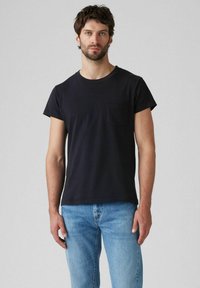 Black short-sleeve T-shirt with a round neckline and a small chest pocket, made of soft cotton fabric, paired with light blue jeans.