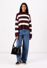 Gestreifter, maroon-weißer, kurzer Pullover, lockere blaue Jeans und eine schwarze Handtasche mit Verschluss. Die Schuhe sind gestreift in Schwarz und Creme.