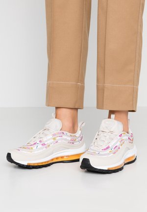 Witte sneakers met kleurrijke bloemenpatronen aan de zijkanten, oranje luchtkussenzolen, gedragen met beige cropped broek.
