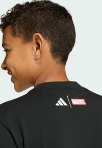 Black cotton t-shirt featuring a round neckline, with white Adidas logo and red Marvel logo printed on the back. Short-sleeve design.