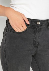 Mustat farkut, joissa on klassinen muotoilu, kapea leikkaus, viisi taskua ja metallinen nappikiinnitys vyötäröllä. Pehmeä farkkukangas.