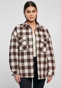 Camisa overshirt a cuadros marrones y blancos con botones en la parte delantera, dos bolsillos en el pecho y un corte relajado. Fabricada con una tela texturada.