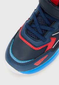 Navy blue sneaker toe with red and light blue accents, navy blue laces, mesh fabric, and a white sole on a white background.