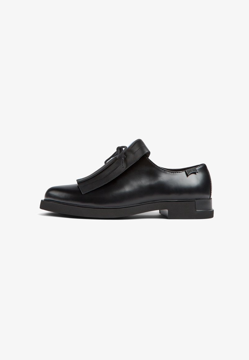 Mocassin en cuir noir à enfiler avec détail de franges et un nœud en dentelle sur le dessus, doté d'un petit talon et d'une finition lisse.