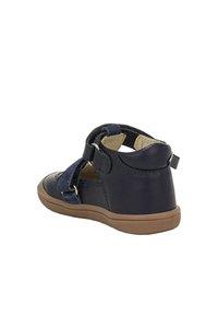 Scarpa in pelle blu navy con cinturino in velcro, punta rotonda e suola in gomma color beige. Presenta morbidi dettagli in camoscio e un tallone imbottito per il comfort.