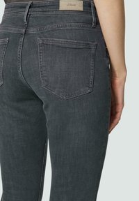 Jean en denim gris foncé avec une coupe slim. Comprend deux poches arrière et une étiquette sur la ceinture. Texture lisse avec des détails de coutures subtils.