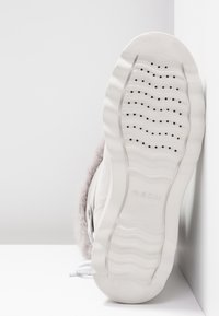 Sneaker bianco con suola in gomma testurizzata, multiple aperture per la ventilazione, materiale superiore liscio e accentuazione in pelliccia sul colletto.
