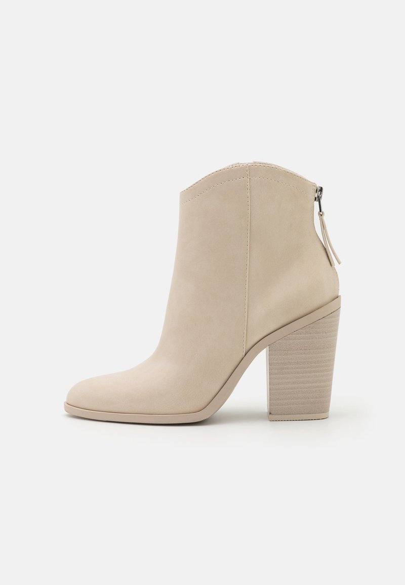 Bottine beige en daim lisse, dotée d'un bout effilé et d'un talon bloc texturé. Fermeture éclair latérale avec détail de languette de tirage.