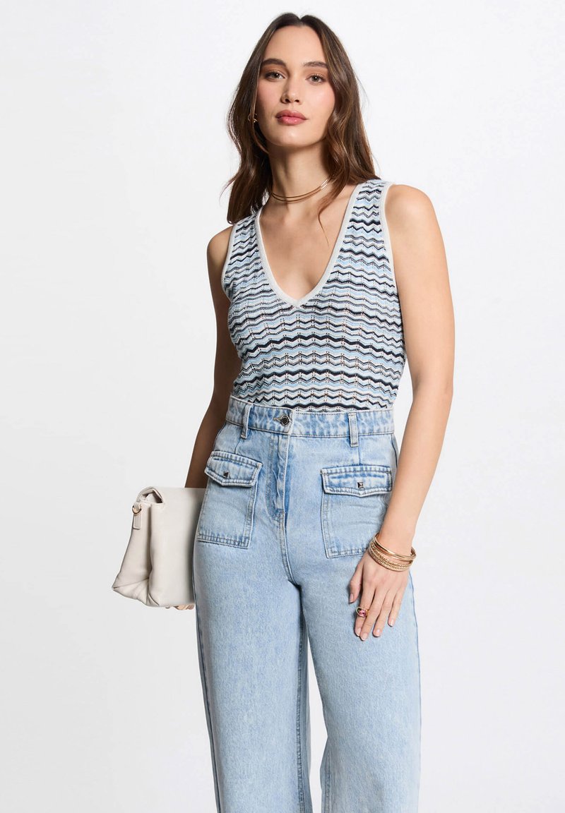 Blauw-witte tanktop met zigzagpatroon en v-hals, gecombineerd met hooggewaisted lichtblauwe denim jeans met zijzakken.