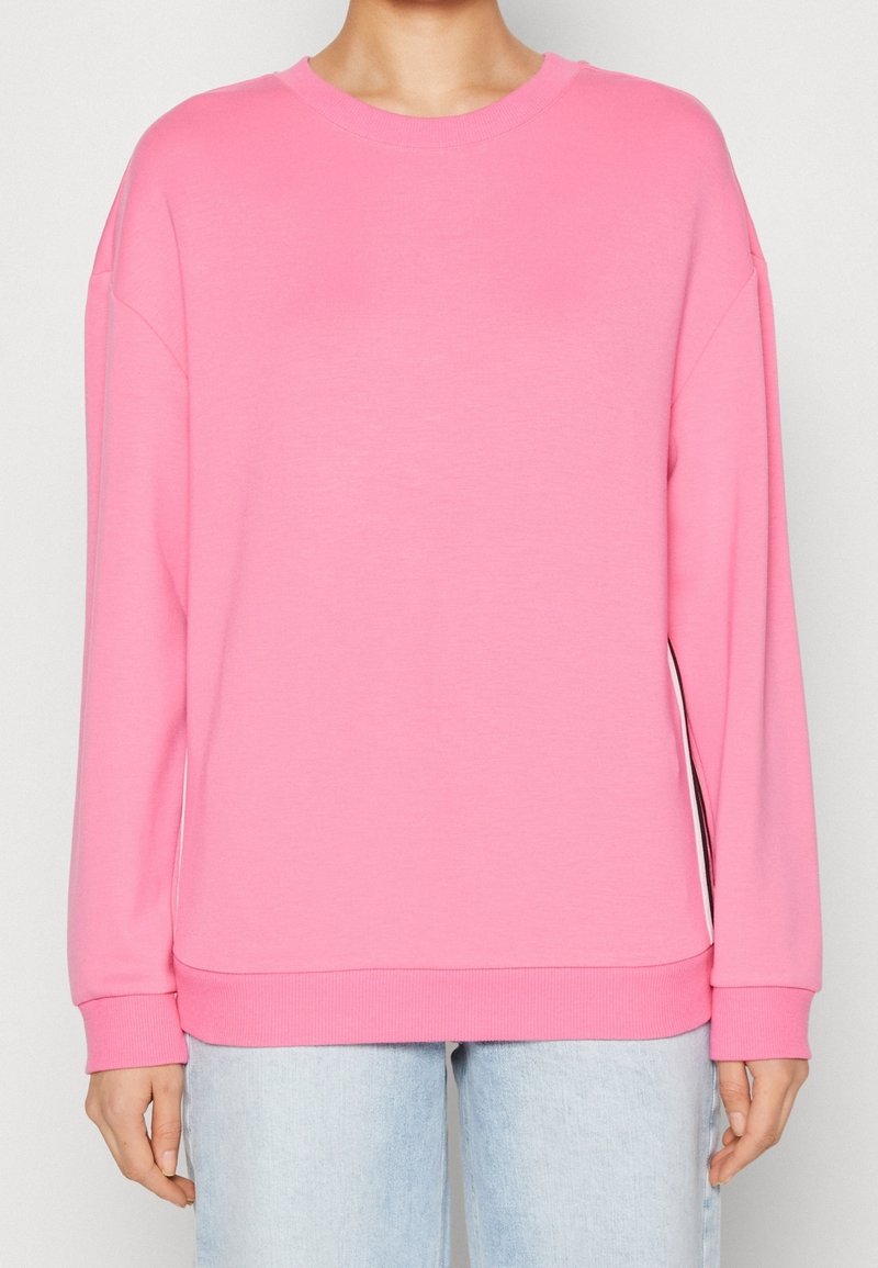 Sudadera de manga larga rosa con hombros caídos, escote redondo y puños acanalados. Textura suave con un diseño de ajuste relajado.
