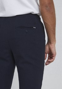 Marineblauwe linnen broeken met een getailleerde taille, elastische band en een enkele knoopzak aan de achterkant met een kleine decoratieve accent.