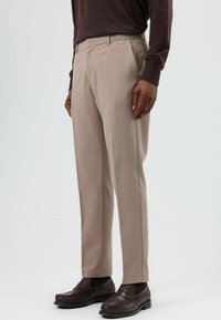 Beige op maat gemaakte broek van gladde stof, met geplooide voorkanten en zijzakken, gecombineerd met donkerbruine mocassins.