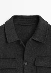 Sort uldblandings skjortejakke med klassisk krave, der har to forreste lommer og knaplukning. Blød tekstur og struktureret design.