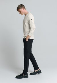 Licht beige sweatshirt met lange mouwen, zwarte op maat gemaakte broek en zwarte instappers. Eenvoudig ontwerp, ribbelboorden en een subtiele logodetail op de mouw.