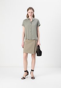 Olive green short-sleeve shirt with button closure, paired with a brown pinstripe skirt and black strappy high-heeled sandals. Black bag accessory.