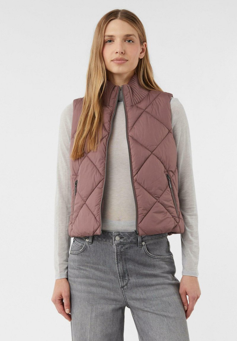 Gepolsterte Weste in Mauve mit hohem Kragen und Reißverschlusstaschen, getragen über einem hellgrauen Langarmshirt und kombiniert mit grauen Jeans.