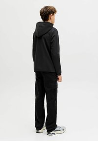 Juodas gobtuvas su gobtuvu, juodos krovinių kelnės, pilki sportbačiai. Sklandus audinys, laisvas kirpimas, funkcionalios šoninės kišenės kelniuose.