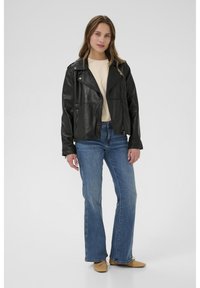 Melnas ādas motokrekls ar asimetrisku rāvējslēdzēju, kabatām ar atloku un norādītu apkakli, saskaņots ar gaiši zilām plati izgriezām biksēm un bēšām čībām.