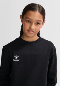 T-shirt a maniche lunghe nera in cotone, con un logo ricamato bianco nella parte sinistra del petto. Design semplice con collo girocollo.