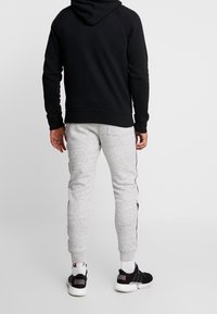 Svart hoodie med huva och raglanärmar, tillsammans med grå sweatpants med strukturerad yta och svarta sidostrikar. Svarta sneakers.