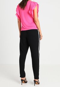 Top rosa de mangas cortas con hombros acampanados, combinado con pantalones negros que tienen rayas blancas en los lados y sandalias negras de tacón alto.