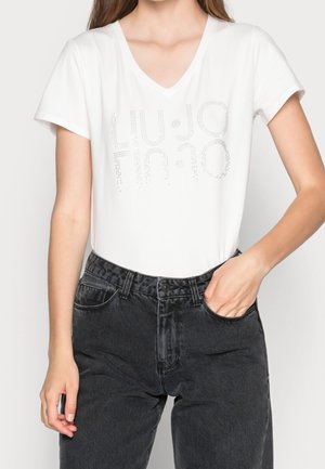 Witte V-hals T-shirt met "LIU JO" in zilverkleurige studs, gecombineerd met hooggetailleerde zwarte jeans. Zachte stof en ontspannen pasvorm.