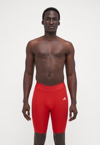 Røde sportsshorts med en tætsiddende pasform, elastisk talje og et hvidt logo på venstre side. Glat, strækbart materiale.
