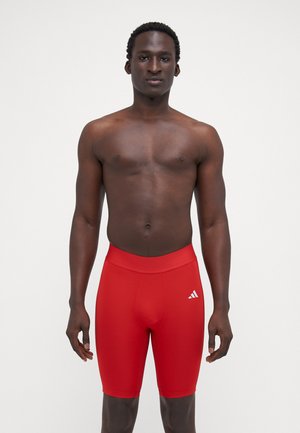 Rode sportieve shorts met een aansluitend ontwerp, elastische tailleband en een wit logo aan de linkerkant. Gladde, rekbare stof.