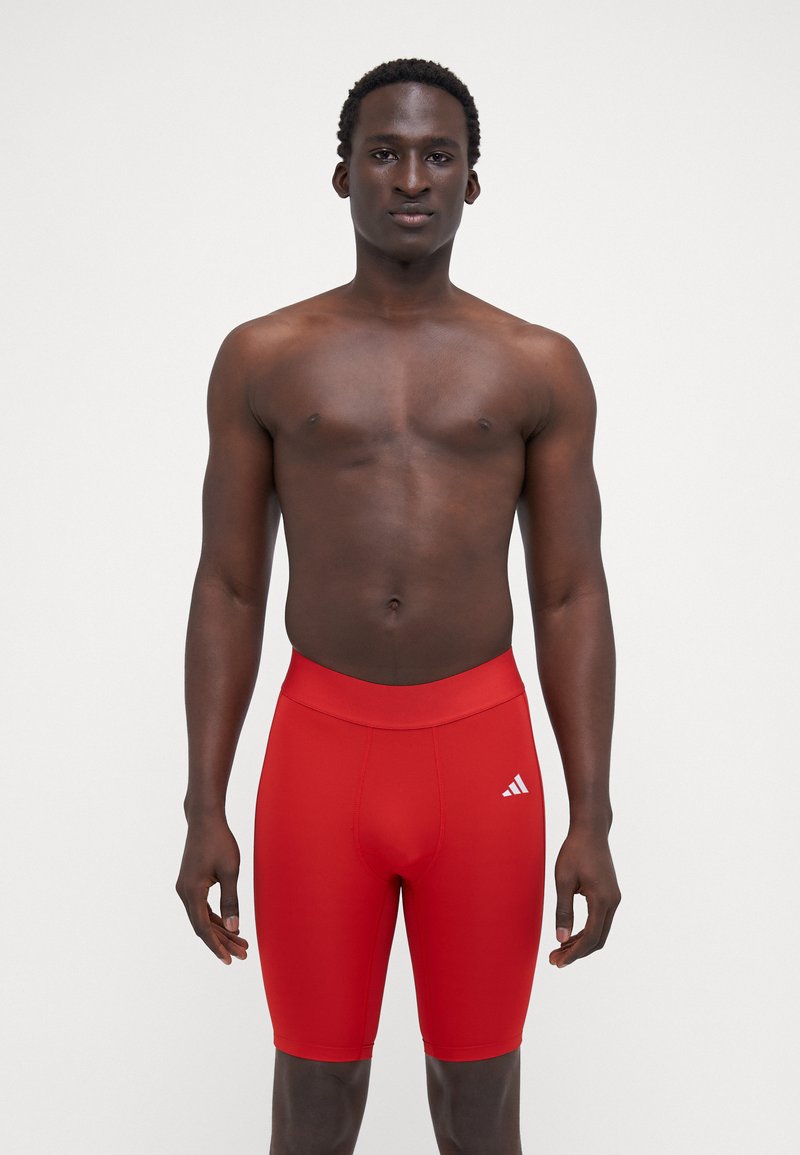 Røde sportsshorts med en tætsiddende pasform, elastisk talje og et hvidt logo på venstre side. Glat, strækbart materiale.