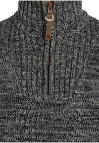 Suéter de punto en gris oscuro con un patrón texturizado. Presenta una media cremallera con herrajes marrones en el cuello para un cierre ajustable.