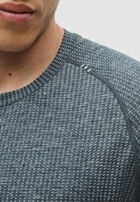 Koszulka sportowa z teksturowanej ciemnoszarej tkaniny z subtelnym geometrycznym wzorem, okrągłym dekoltem i kontrastowymi detalami szwów.