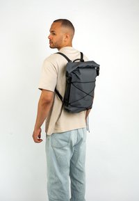 Zaino roll-top grigio con spalline nere regolabili, caratterizzato da un design elegante e tessuto testurizzato, chiuso da un cordino e un meccanismo a scorrimento.