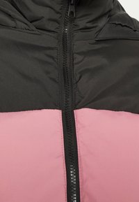 Giacca a vento con una sezione superiore nera e una sezione inferiore rosa, caratterizzata da una zip centrale e una texture liscia e opaca.