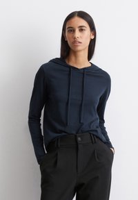 Marineblauwe hoodie met lange mouwen van zachte stof, voorzien van een trekkoord in de capuchon en een ontspannen pasvorm, gecombineerd met op maat gemaakte zwarte broek met voorplooien.