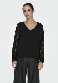 Czarna bluzka z dekoltem w serek i jednolitą sylwetką, mająca przezroczyste koronkowe długie rękawy. Materiał jest lekki, a projekt zawiera elastyczne mankiety.