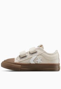 Zapatilla de lona beige con suela de goma marrón, dos tiras de velcro, logo de estrella blanca y costuras en contraste en la parte superior.