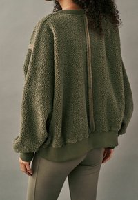 Fuzzy olivengrøn pulloverjakke med tekstureret stof, drop-skuldrer, ribbede manchetter og en central sømdetalje på ryggen.