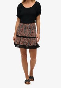 Top corto nero con texture arricciata, abbinato a una mini gonna paisley arancione e blu con bordo in pizzo e dettagli neri. Sandali neri.