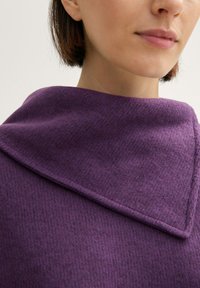 Lila wollene Schal mit einem gefalteten Kragendesign, strukturierter Oberfläche und weicher, warmer Ausstrahlung. Nahaufnahme, die die reiche Farbe und die Stoffdetails zeigt.