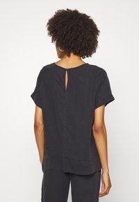 Sort top med korte ærmer og en let løs pasform. Har en nøglehul-åbning bagpå og en kant, der er lidt længere bagtil.