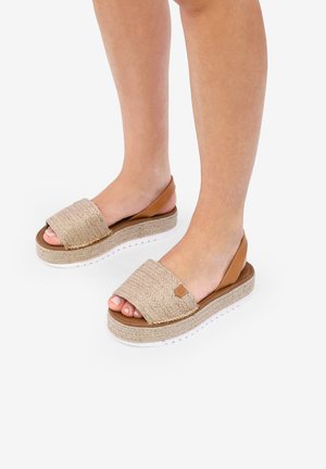 Sandalias de estilo espadrille con una parte superior de tejido beige y acentos de cuero marrón, que cuentan con una suela de goma blanca y un diseño de plataforma.