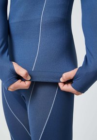 Ropa deportiva en azul marino con tejido texturizado, diseño ajustado y costuras en blanco. Manos sostienen la prenda por el dobladillo para ajustarla.