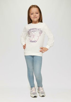 Witte sweatshirt met paarse vlinderafbeelding en tekst "SPARKLE AND SHINE," gecombineerd met blauwe jeans en grijze sneakers.