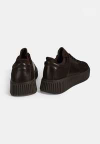 Braune Ledersneaker mit strukturierter Oberfläche, ausgestattet mit einer geriffelten Laufsohle und Schnürdesign. Auf der Rückseite befindet sich ein glattes Akzentpanel.