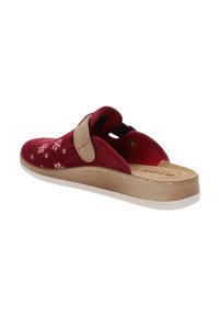 Scarpa slip-on rossa con cinturino beige, motivo a fiocchi di neve e suola in texture legno, inclinata per mostrare il lato interno e il retro.
