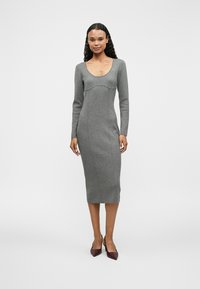 Robe midi grise à manches longues avec un décolleté rond, un corsage ajusté et des détails de coutures, complétée par des escarpins pointus bordeaux.